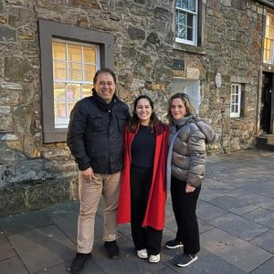 A family comprising parents with their university-age daughter in the centre, standing on a historic street.